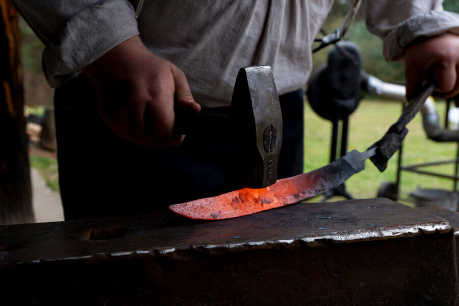 Hidden History in the Southβs Most Beautiful State Parks - 5 A person hammers a glowing hot metal blade on an anvil, shaping it as part of a blacksmithing process.