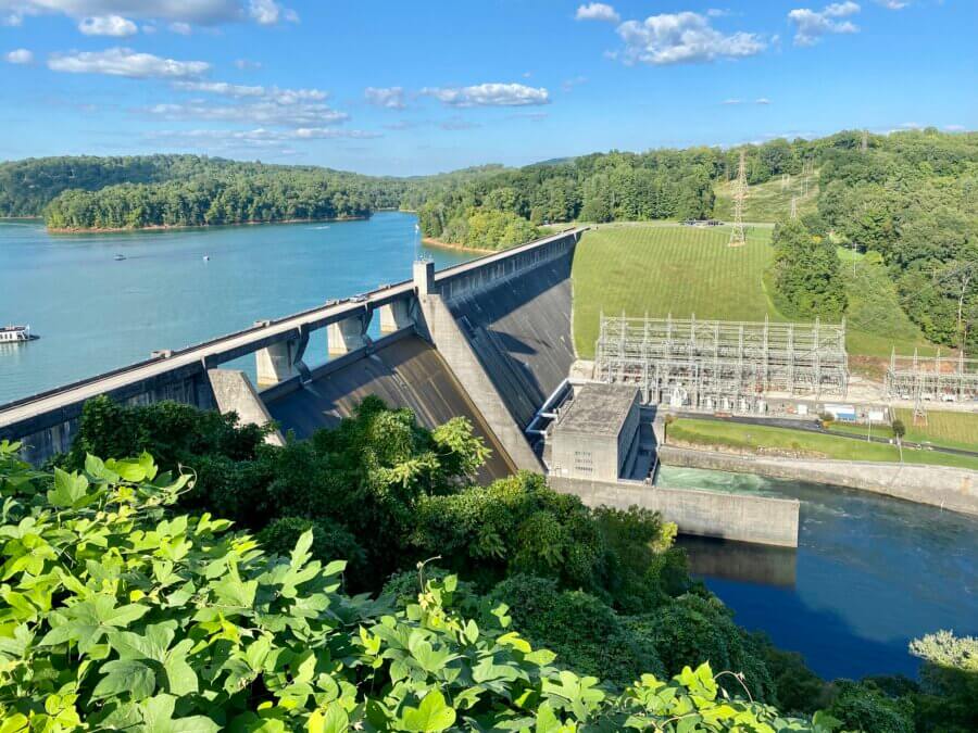 Hidden History in the Southβs Most Beautiful State Parks - 9 A large concrete dam with electrical infrastructure sits beside a river and forested hills under a blue sky.