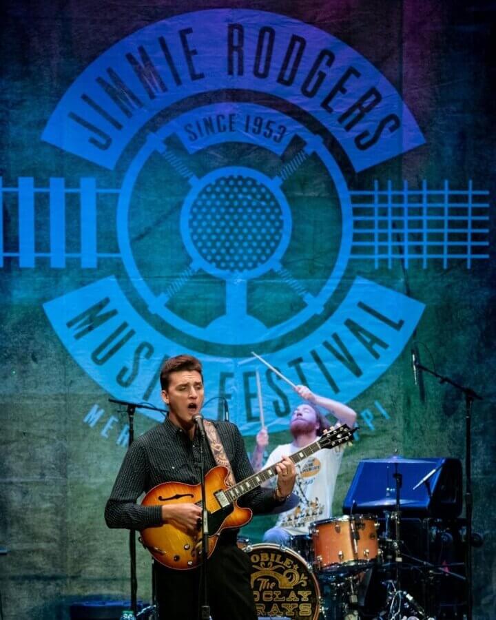 16 Can't-Miss Events in Meridian, MS This Season - 5 A musician plays an electric guitar and sings on stage while a drummer performs behind him at the Jimmie Rodgers Music Festival, one of the top things to do in Meridian and a highlight among Meridian MS events.