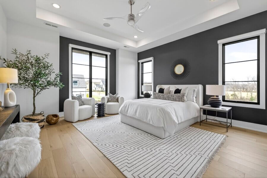 Just Listed! A Custom Williamson County Home Where Indoor & Outdoor Living Shine - 13 Modern bedroom in a custom home with a white bed, geometric rug, black accent wall, three windows, two white armchairs, potted plant, and minimalistic decorβperfect for embracing indoor-outdoor living in Williamson County.