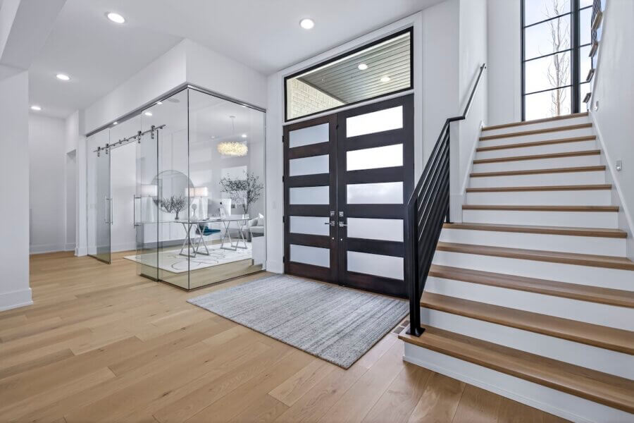 Just Listed! A Custom Williamson County Home Where Indoor & Outdoor Living Shine - 3 Modern custom home entryway with wooden stairs, glass-walled office on the left, large geometric front door, and light wood flooring throughout this stunning Williamson County home.