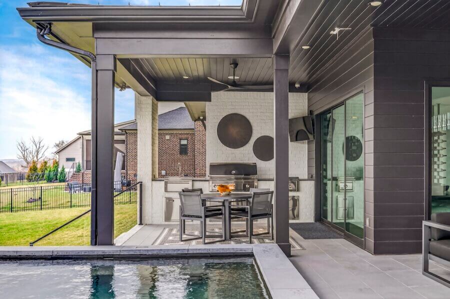 Just Listed! A Custom Williamson County Home Where Indoor & Outdoor Living Shine - 6 Experience seamless indoor outdoor living on this covered patio, featuring a dining table, grill, and ceiling fan beside the poolβperfect for a Williamson County home with lawn views and neighboring houses in the background.