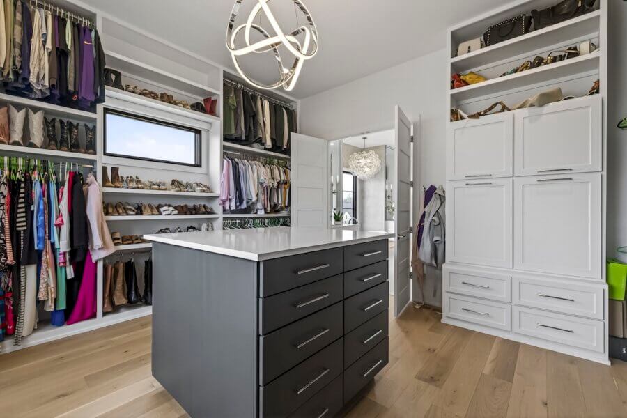 Just Listed! A Custom Williamson County Home Where Indoor & Outdoor Living Shine - 11 Modern walk-in closet with open shelves, hanging clothes, shoes, white cabinetry, and a central island with drawers beneath a contemporary light fixtureβperfect for a custom home in Williamson County.