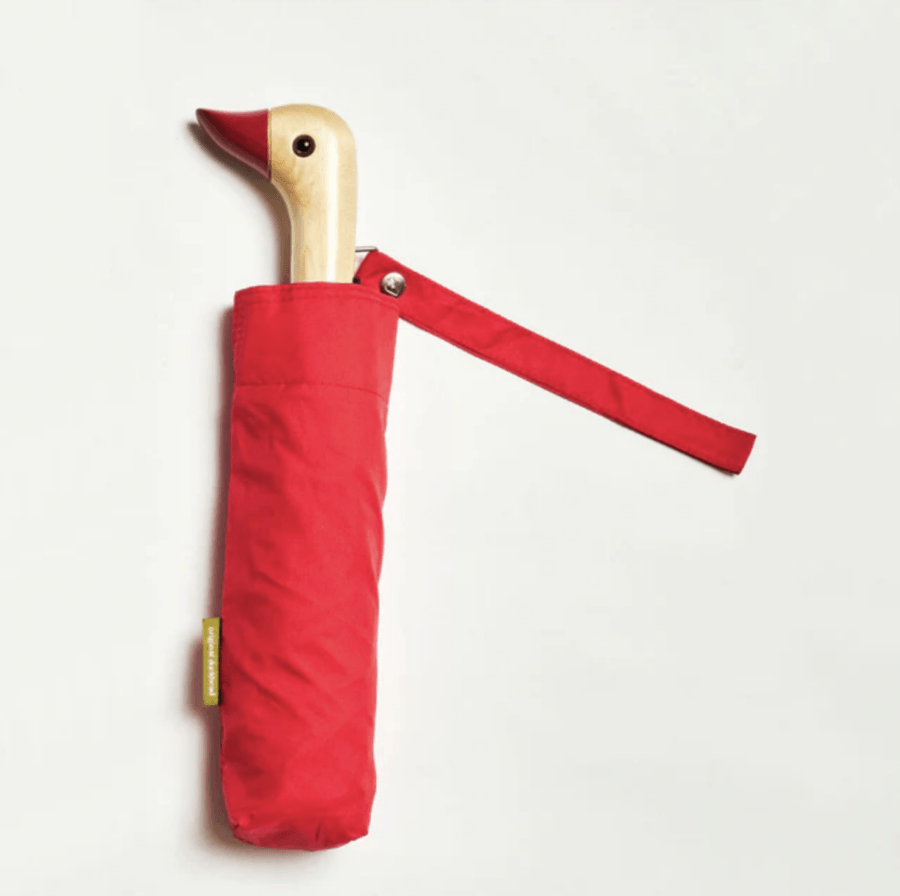 A red umbrella with a wooden handle shaped like a duck's head, partially enclosed in a matching red sleeve, stands ready for April showers—perfectly complementing your chic rainwear against a plain background.