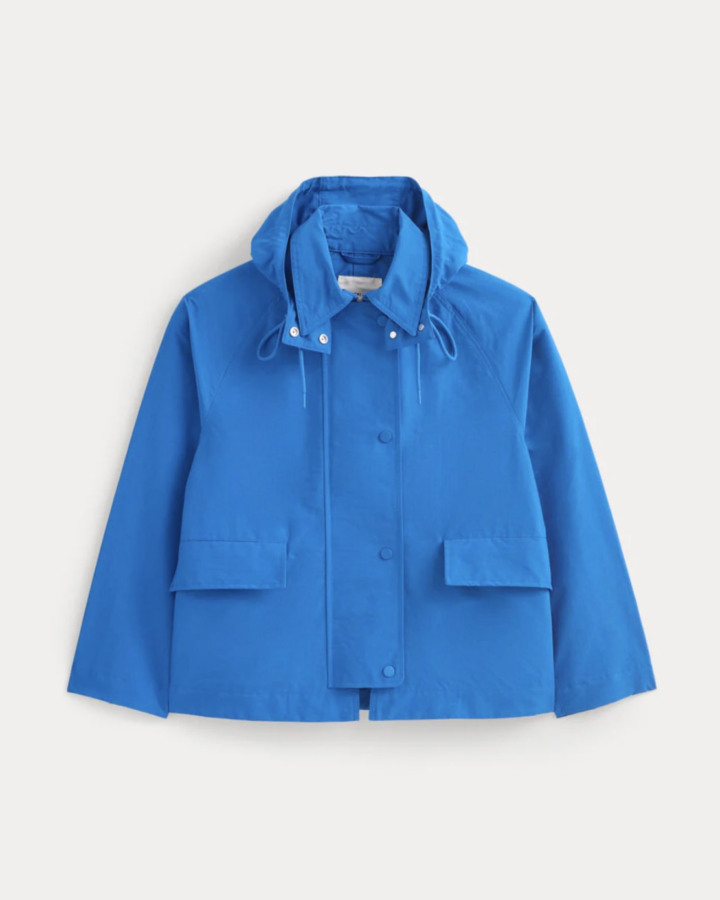 Bright blue hooded jacket with front snap buttons, two large flap pockets, and drawstrings at the hood—perfect chic rainwear for staying stylish during April showers. Displayed on a plain background.