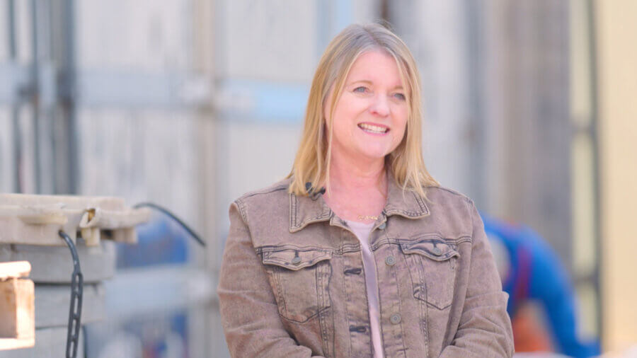 Meet the Woman Keeping Florida’s Oldest Fishing Village Thriving - 2 A woman with shoulder-length blonde hair, wearing a brown jacket, stands outdoors smiling with a blurred background.