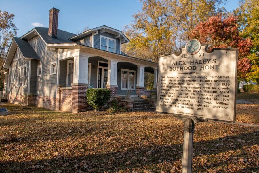 Living History: 7 Tennessee Towns Where the Past Comes Alive - 5 A historical marker stands before Alex Haley’s Boyhood Home, a gray house with a porch, surrounded by autumn trees and fallen leaves — a glimpse into living history in one of Tennessee's notable historic towns.
