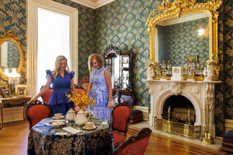 Living History: 7 Tennessee Towns Where the Past Comes Alive - 3 Two women stand in a lavish, antique-furnished room with ornate wallpaper, a large gold mirror, and a marble fireplace — an elegant scene of living history.