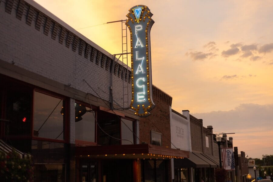 Living History: 7 Tennessee Towns Where the Past Comes Alive - 7 A neon sign reading "Palace" is mounted vertically on the facade of a building along a row of storefronts at sunset, capturing the charm of historic Tennessee towns.