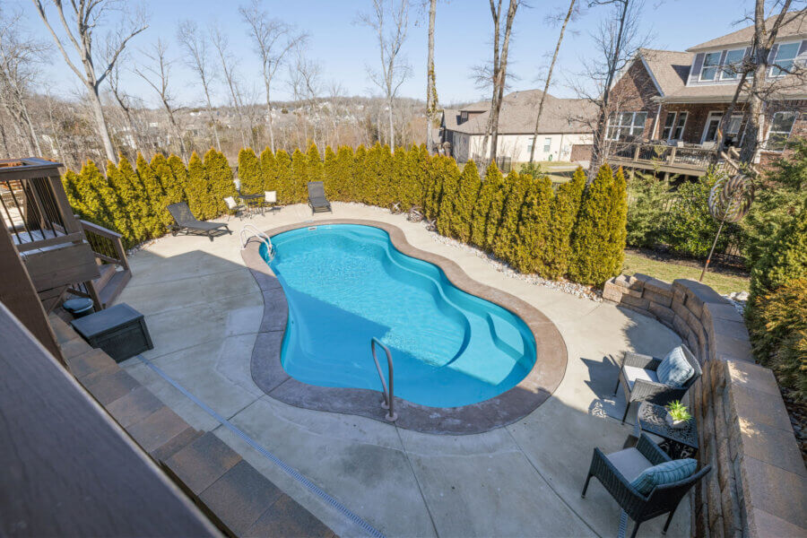 Just Listed! This Nolensville Home is Ready for Summer Entertaining - 9 Just Listed! This Nolensville home features an outdoor kidney-shaped swimming pool, perfect for summer entertaining, with a concrete patio, lounge chairs, lush shrubs, and nearby houses under a clear sky.
