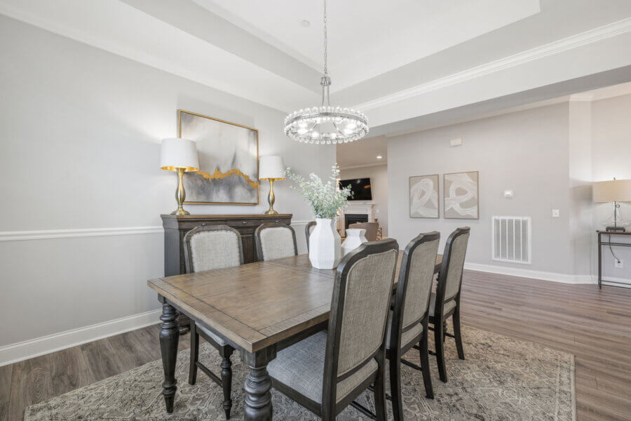 Just Listed! This Nolensville Home is Ready for Summer Entertaining - 4 A Nolensville Home dining room with a wooden table, six upholstered chairs, a modern chandelier, sideboard, lamps, and abstract wall art on light gray walls—perfect for summer entertaining.