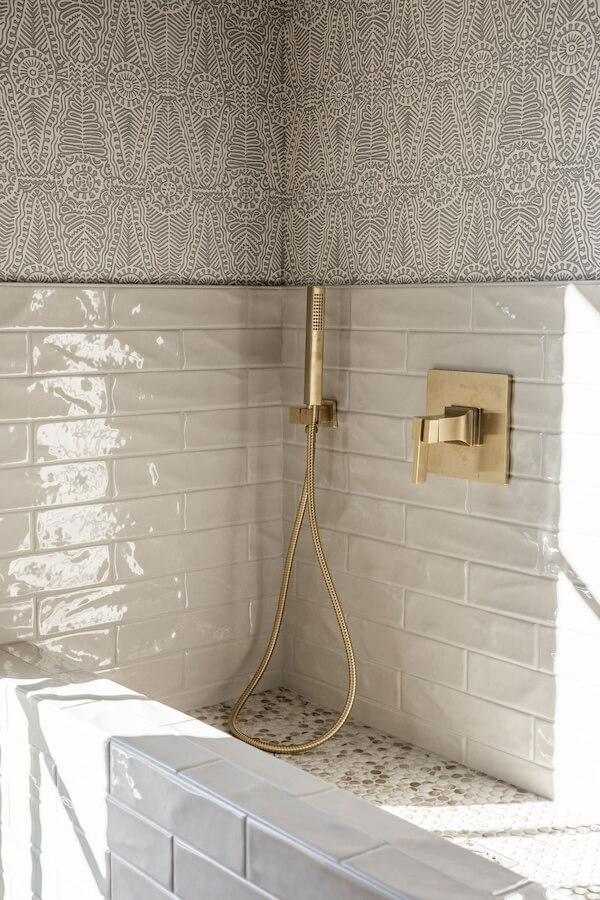 7 Tile Trends Interior Designers Are Loving Right Now - 24 A shower corner with white subway tiles—a nod to tile trends—patterned wallpaper above, and brass fixtures including a hand shower and control handle.