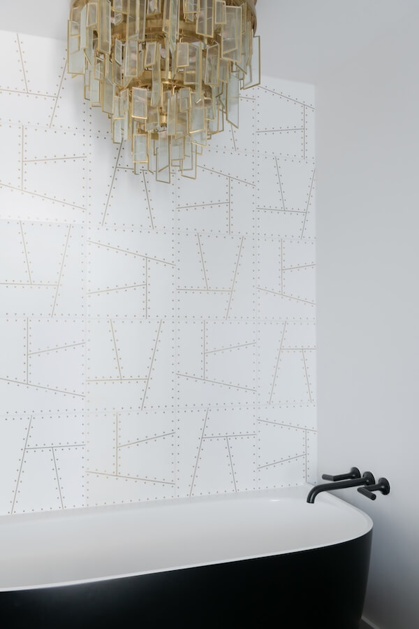 7 Tile Trends Interior Designers Are Loving Right Now - 12 A modern bathroom featuring a black and white bathtub, geometric patterned wall reflecting the latest tile trends, a black faucet, and a hanging glass chandelier.