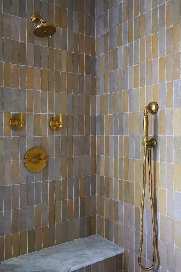 7 Tile Trends Interior Designers Are Loving Right Now - 21 Shower with tan square tiles that showcase the latest tile trends, brass fixtures, a fixed showerhead, a handheld showerhead, and a built-in marble bench.