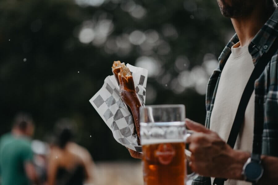 The Best Festivals in the South - 23 A person holding a large pretzel in a paper wrapper and a glass of beer outdoors, with people blurred in the background—capturing the lively spirit of Southern festivals and some of the Best Festivals in the South.
