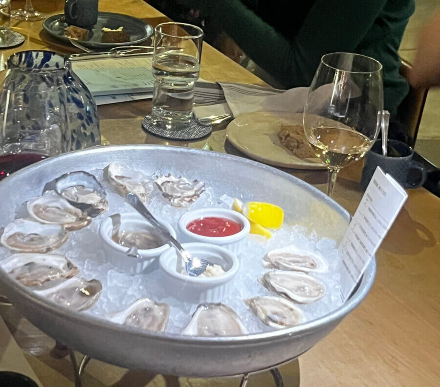 Your Guide to Chattanooga's Culinary Scene - 6 A metal tray of raw oysters on ice with lemon, cocktail sauce, and horseradish sits on a wooden table set for dining in Chattanooga, complete with plates, glasses, and utensils.