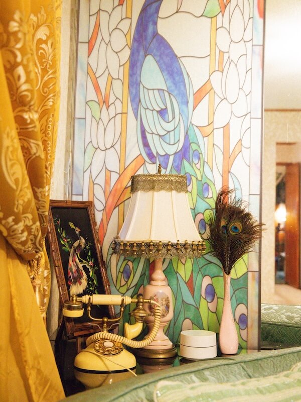 Lil' Graceland: An Elvis-Inspired Retreat Just Minutes from the Real Deal - 6 A vintage lamp, rotary phone, peacock feather, and framed art sit on a table in front of a stained-glass peacock mural at Lil Graceland.