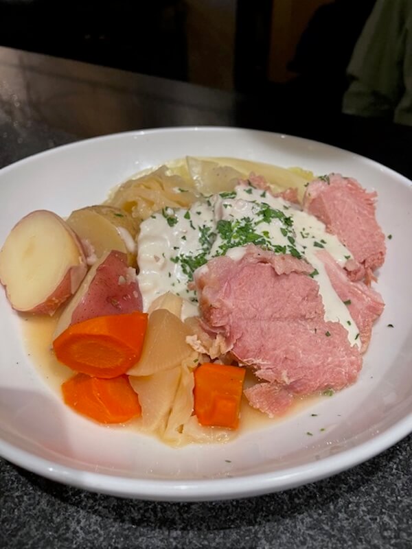 The Best Irish Pubs in Nashville - 4 A white bowl containing slices of corned beef with cream sauce, red potatoes, carrots, cabbage, and a sprinkle of parsley.
