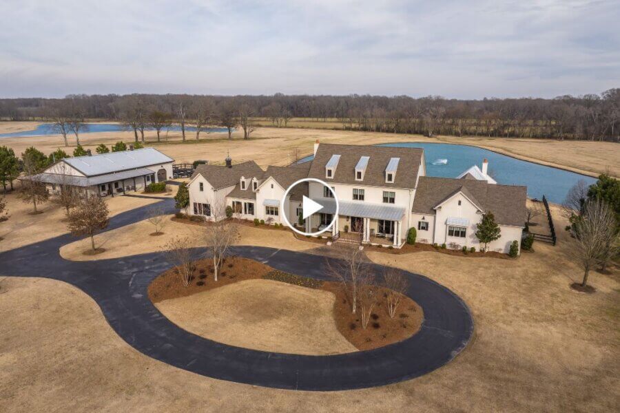 Aerial view of a large white house with a circular driveway at 770 Ballard Rd, Piperton TN, featuring a nearby pond, barn-like building, and expansive open land.