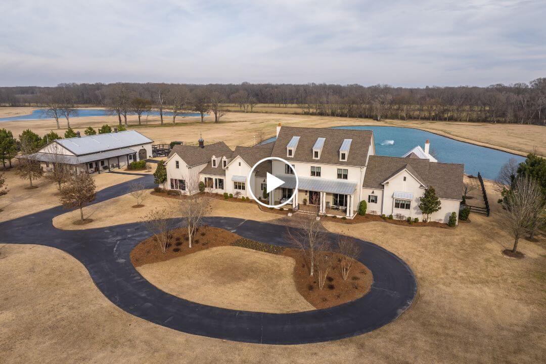 Aerial view of a large white house with a circular driveway at 770 Ballard Rd, Piperton TN, featuring a nearby pond, barn-like building, and expansive open land.