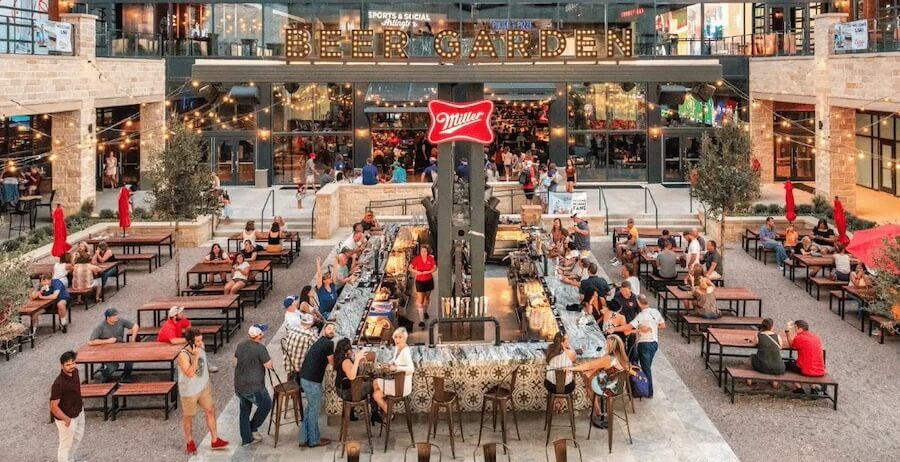 The Southerner's Guide to the 2026 World Cup - 5 Outdoor beer garden with people sitting at picnic tables and a central bar, surrounded by string lights and a large "BEER GARDEN" sign above the entrance—an ideal spot to catch the World Cup matches with friends.