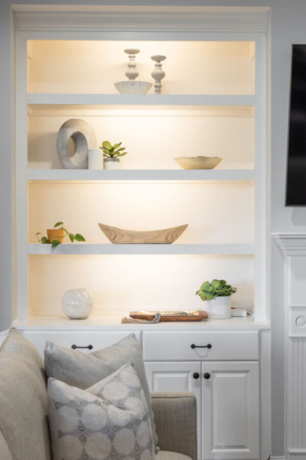 Just Listed! This Nolensville Home is Ready for Summer Entertaining - 6 Built-in white shelves in this Nolensville Home display decorative objects, small potted plants, and bowls above white cabinets next to a beige sofa with patterned pillows—perfect for summer entertaining.