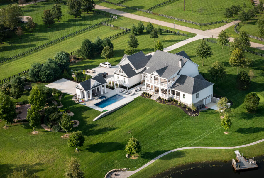Why the South's Top Home Builders Use C3 Studio - 4 Aerial view of a large modern house with a swimming pool, patio, and manicured lawn—showcasing custom home design services—surrounded by trees and a pond in a peaceful rural setting.