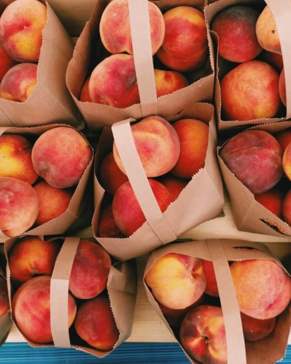 Brown paper bags filled with ripe peaches are arranged closely together on a wooden surface, evoking the charm of local markets at the best festivals in the South.