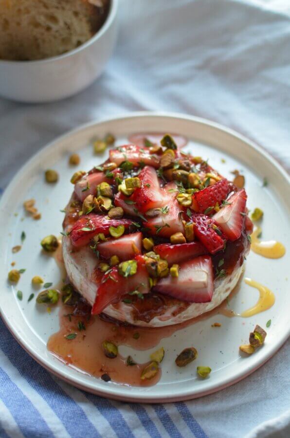 3 Quick and Easy Appetizers for Spring - 3 A round cheese topped with sliced strawberries, chopped pistachios, and a drizzle of syrup on a white plate, with a piece of bread in the background.