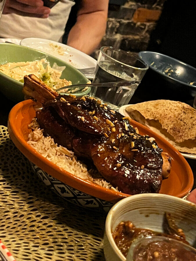 Your Guide to Chattanooga's Culinary Scene - 7 A glazed lamb shank served on rice in a brown dish, accompanied by bread, salad, and various side dishes on a Chattanooga restaurant table.