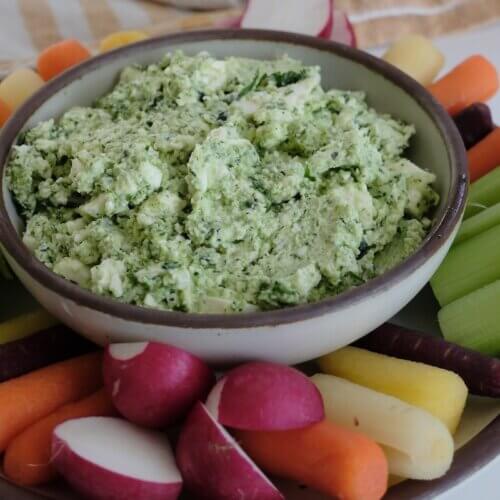 RECIPE: Herby Feta Dip - 3 A bowl of herbed cheese dip is surrounded by celery, carrots, and radishes arranged on a plate.