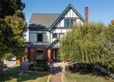 A two-story Tudor-style house at 903 Russell St, Nashville TN, features white and dark trim, brick accents, a front porch, and mature trees in the yard on a clear day.