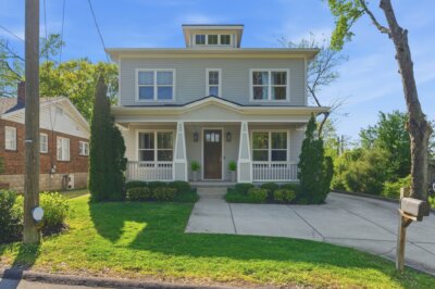 Charming two-story house with gray siding, white trim, a covered front porch, symmetrical windows, driveway, and neatly landscaped yard on a sunny day in the heart of 44th Ave N Nashville, TN.