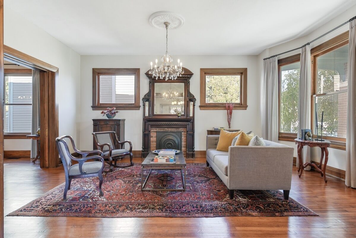 Charming living room at 903 Russell St, Nashville, with wooden floors, antique fireplace, chandelier, upholstered sofa, two armchairs, coffee table, and large windows that fill the space with natural light.