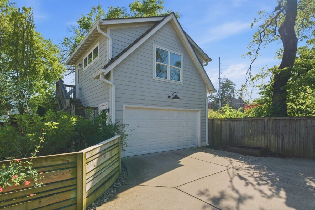 Charming two-story gray house at 98 44th Ave N with a white garage door, wooden fence, mature trees, and a paved driveway under a clear blue sky.