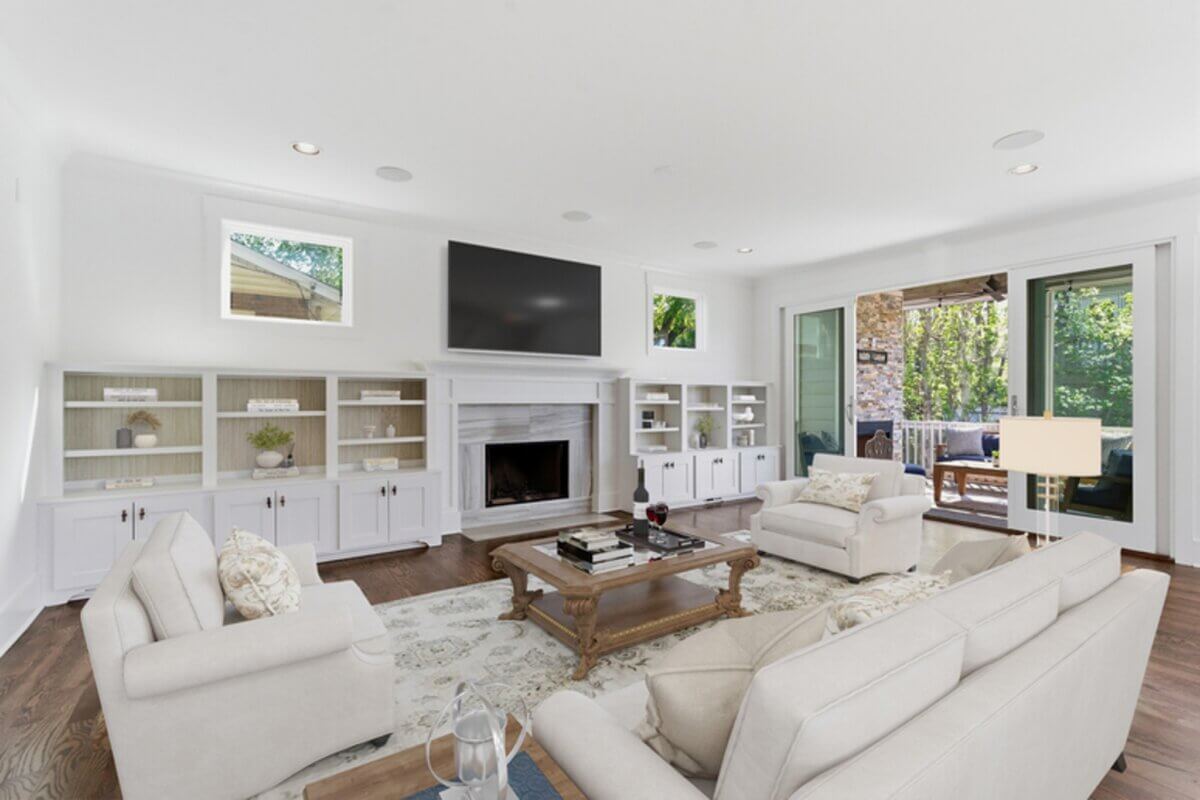 Spacious living room with white walls, built-in shelves, a fireplace, large TV, beige sofas, coffee table, and sliding doors opening to a patio with outdoor seating—perfect for relaxing at 98 44th Ave N in Nashville.