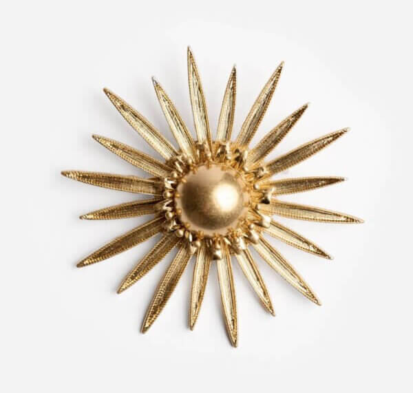 It's the Year of the Brooch! Here's How to Style Them - 3 Gold sunburst brooch with a round center and textured, pointed rays extending outward, showcased among elegant brooches on a white background.