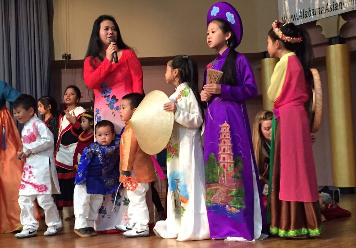 From War Refugee to Biochemist to ... Tap Dancer! Meet Helen Kim - 5 A group of children and adults in traditional Asian clothing stand on a stage at the AL Asian Cultures Foundation event.