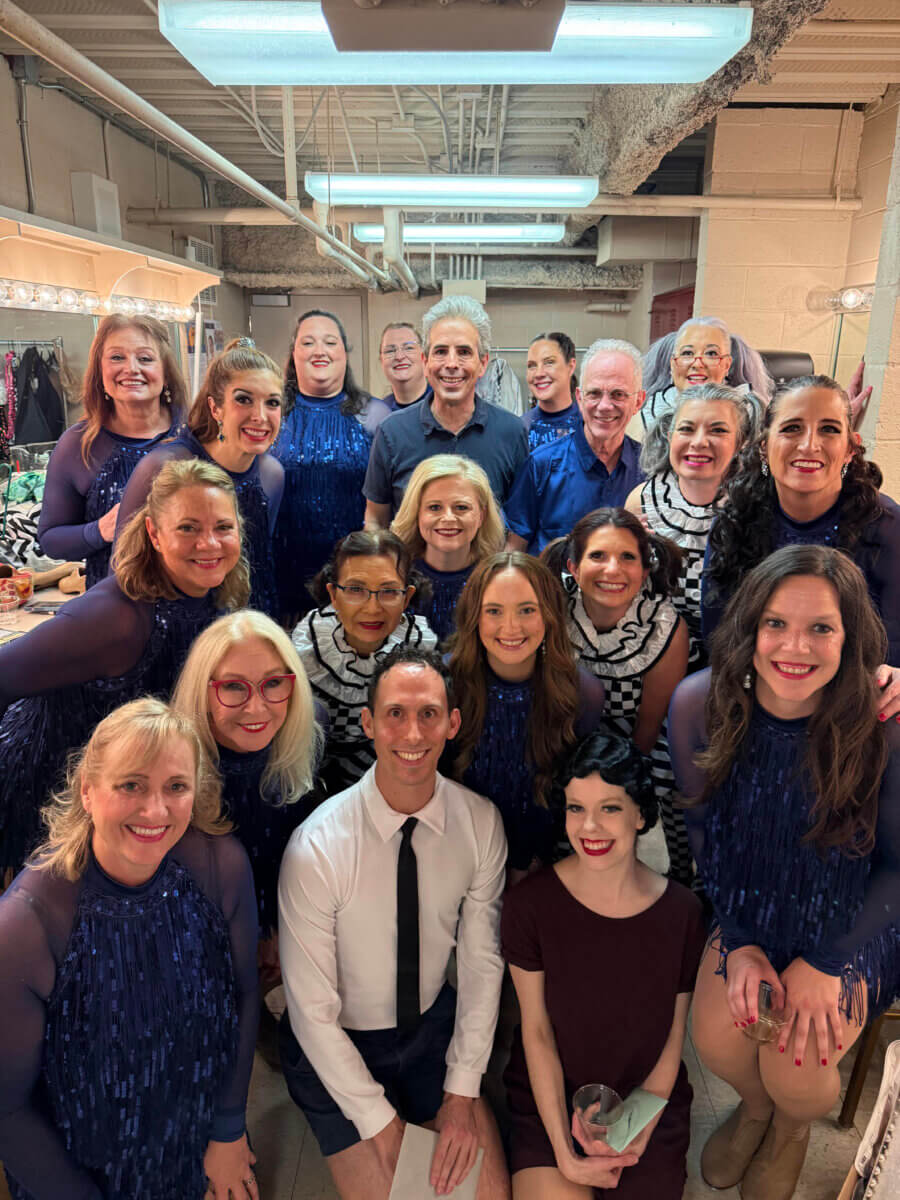 From War Refugee to Biochemist to ... Tap Dancer! Meet Helen Kim - 7 A group of performers in costumes poses together backstage, smiling for the camera in a well-lit dressing room, celebrating unity in diversity inspired by Asian cultures.