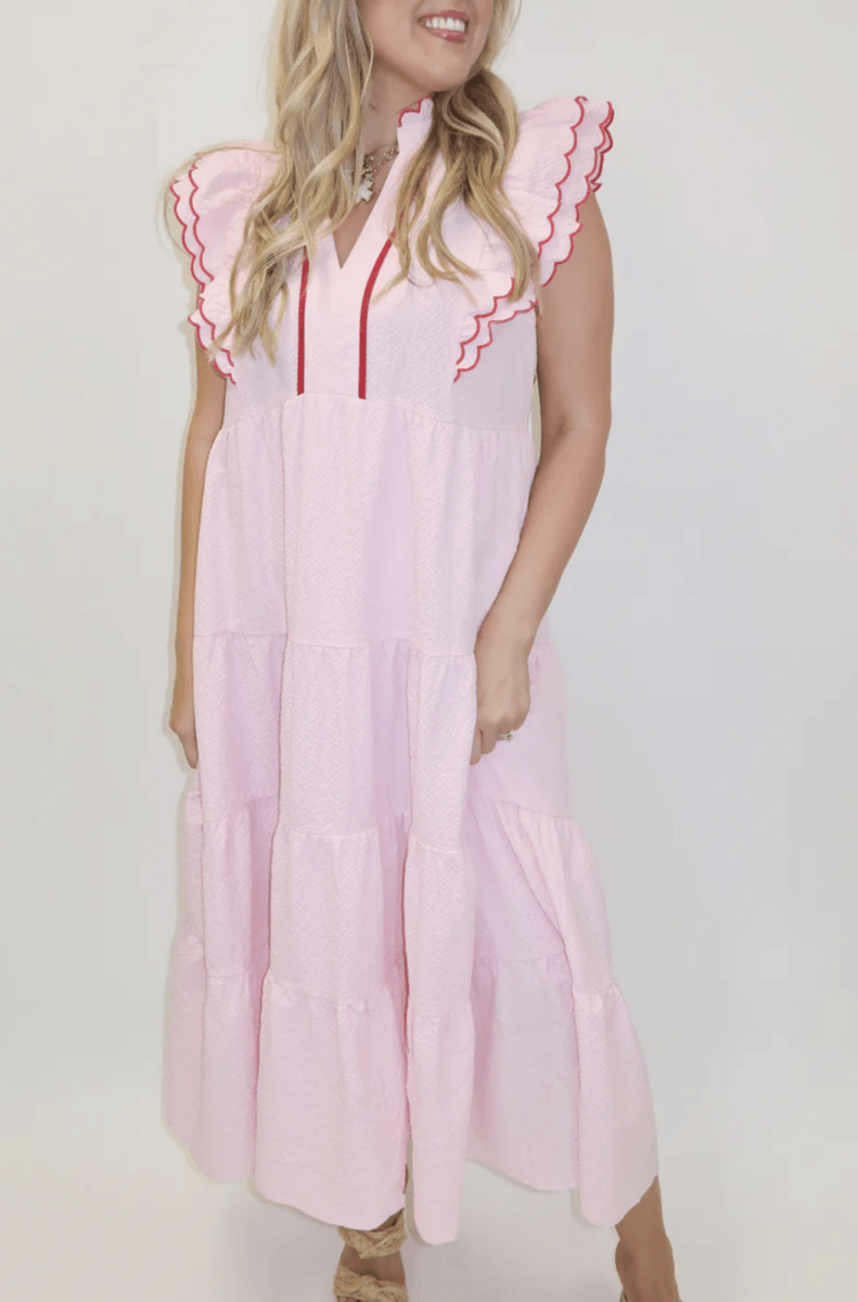 18 Birmingham FINDS for May Celebrations: Graduation, Mother's Day & More - 2 Woman wearing a light pink, tiered maxi dress with scalloped cap sleeves and red trim, standing against a plain white background.
