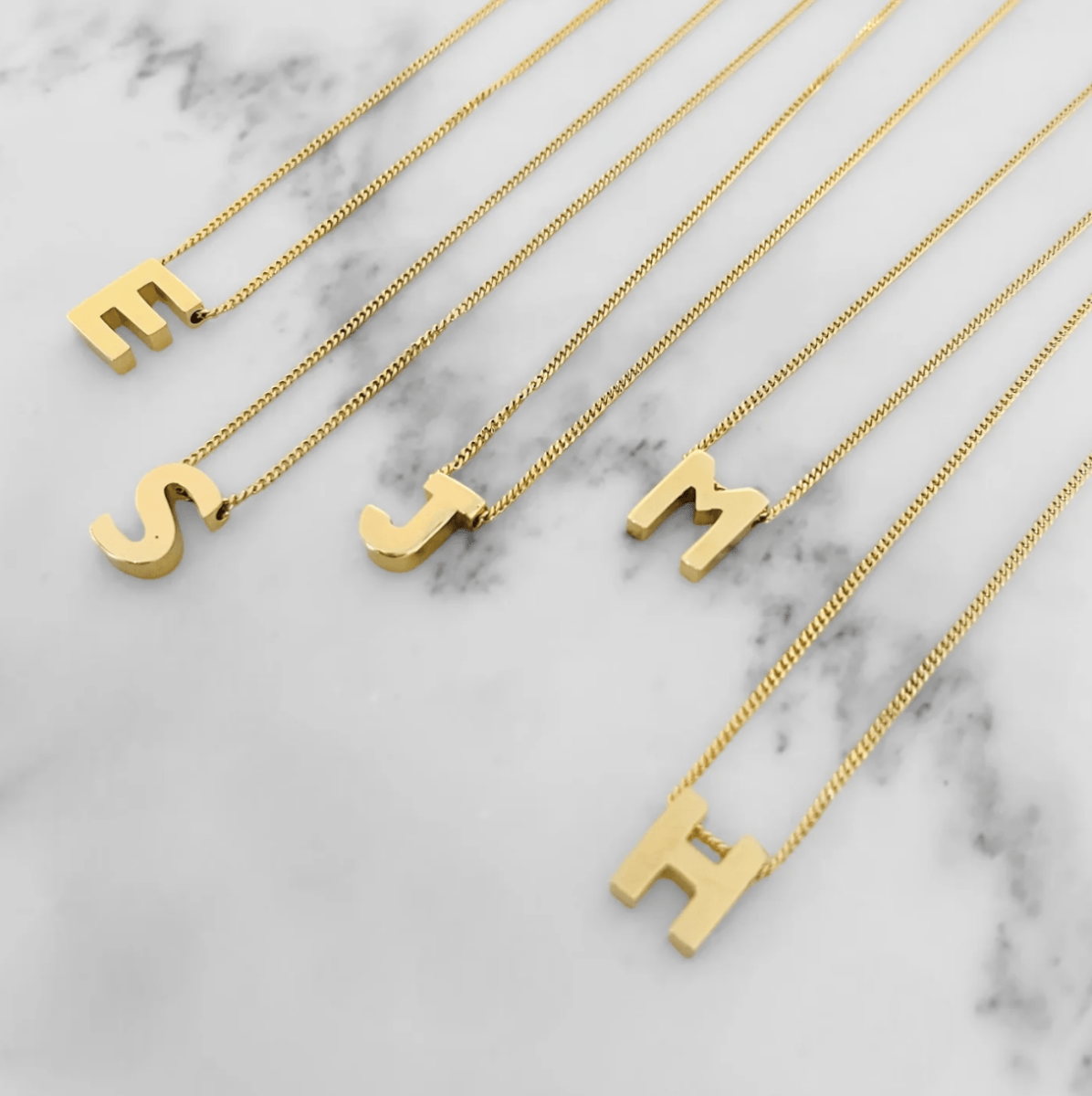 18 Birmingham FINDS for May Celebrations: Graduation, Mother's Day & More - 10 Five gold necklaces with chain links, each featuring a pendant in the shape of a letter: E, S, J, M, and H, displayed on a white marble surface.