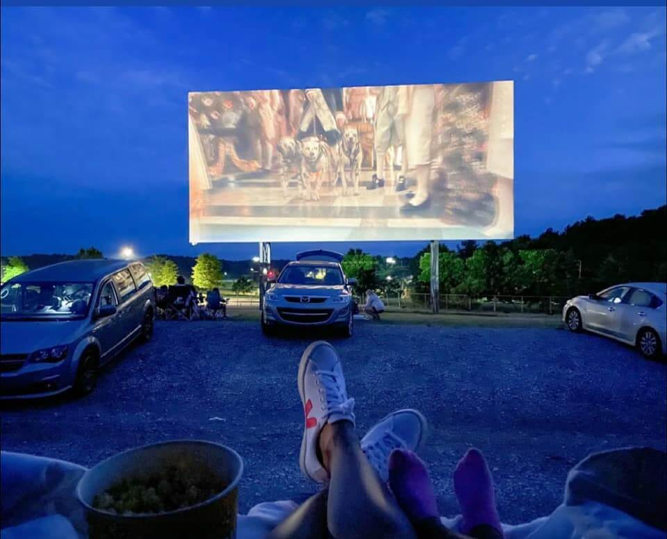 View from inside a car at a Birmingham outdoor movie event at dusk, showing people relaxing with their feet up and a film playing on the big screen—perfect for your ultimate outdoor movie guide.