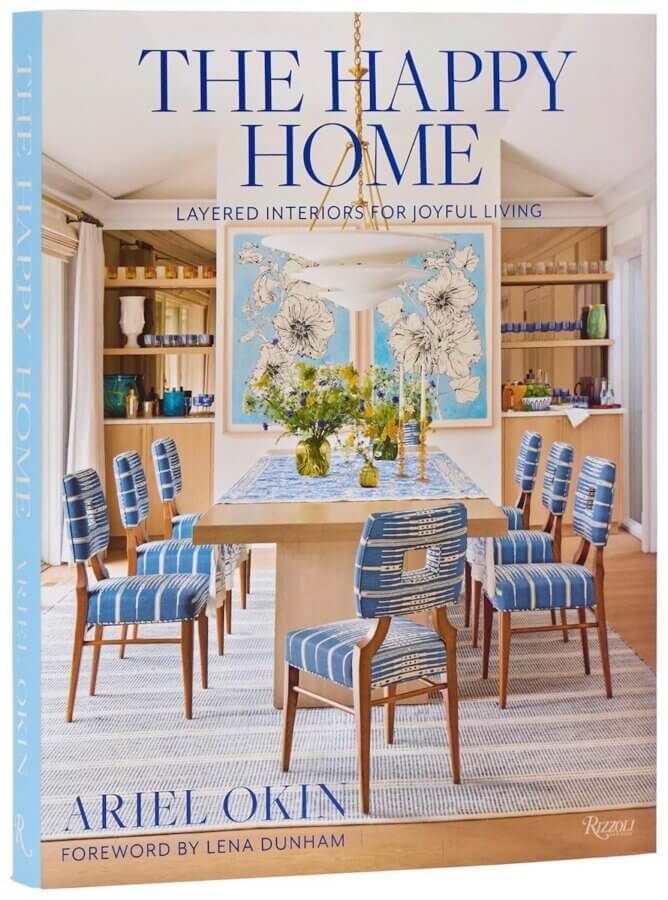 9 New Design-Forward Coffee Table Books for Your Wish List - 2 Book cover of "The Happy Home" by Ariel Okin—sure to spark design envy—features a modern dining room with blue-striped chairs, a wooden table, and minimalist decor; a must-have coffee table book among 2026 releases.