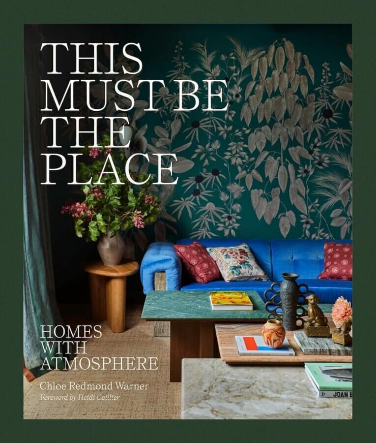 9 New Design-Forward Coffee Table Books for Your Wish List - 7 Book cover for "This Must Be The Place: Homes with Atmosphere," a 2026 release and future coffee table book, featuring a living room with a blue sofa, green leafy wallpaper, and a wooden coffee table.