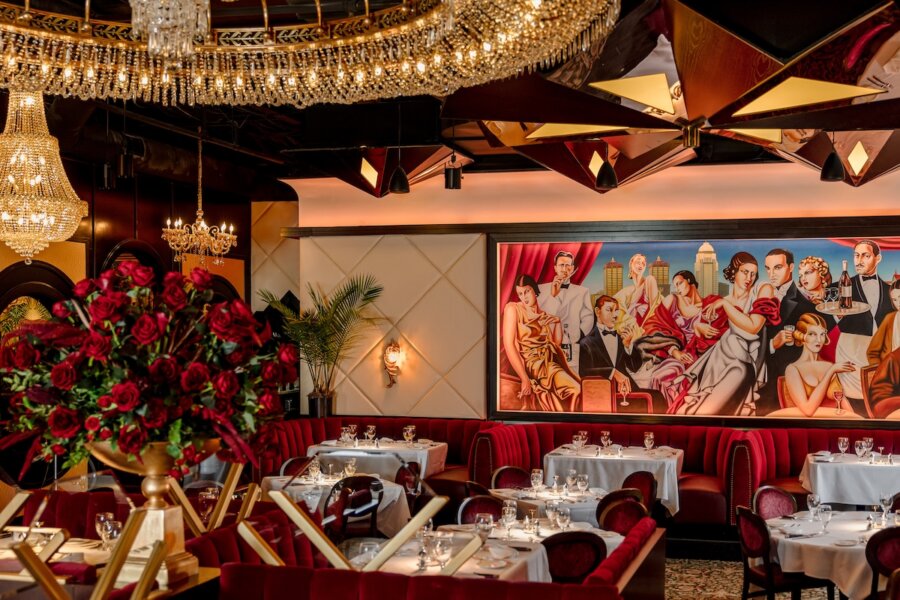 All-Ages Adventure: The Ultimate Trip to Louisville, KY - 17 Elegant restaurant interior with red velvet seating, white tablecloths, chandeliers, floral arrangements, and a large mural of formally dressed people—an ideal spot among the top things to do in Louisville.