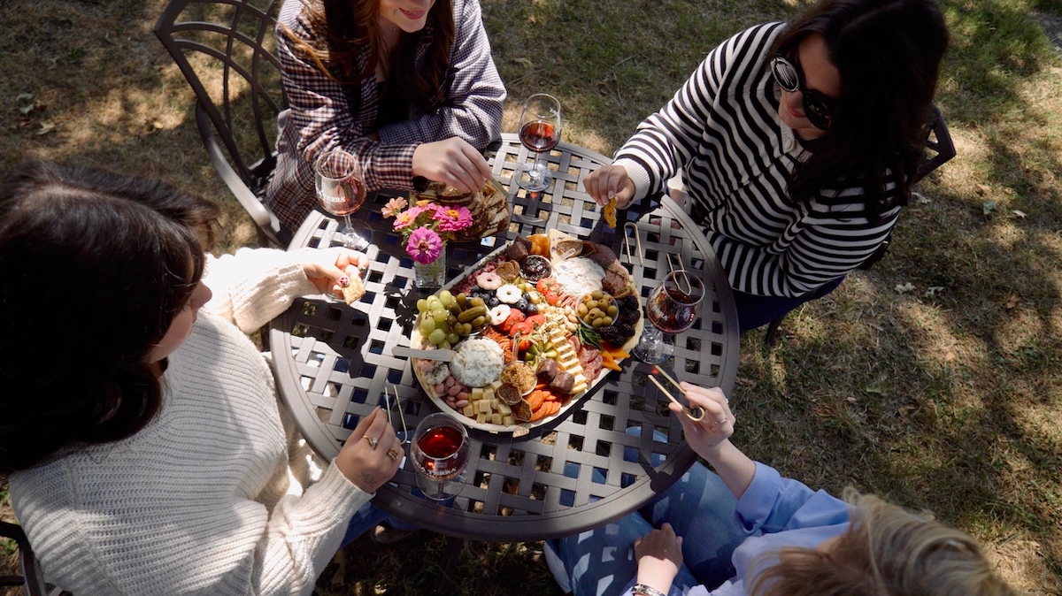 6 Southern Waterfront Weekend Escapes - 13 Four people sit around a metal patio table outdoors, sharing a charcuterie board and glasses of red wine, enjoying the relaxed atmosphere typical of waterfront vacations.