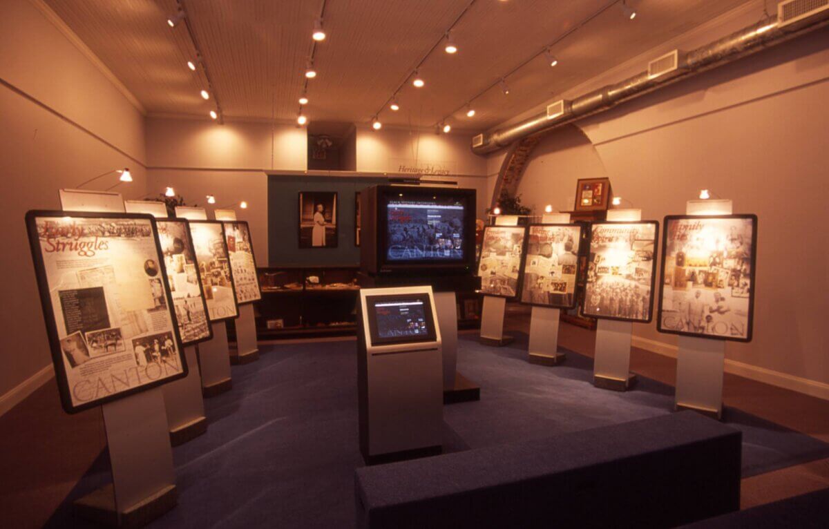 A dimly lit exhibition room with standing display panels, a central digital screen, and historical photographs and documents on the walls—an inspiring stop for Southern family vacation seekers hunting kid-tested destinations and parent-approved travel experiences.