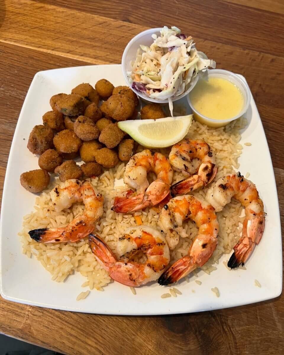 A plate with grilled shrimp on rice, fried okra, a lemon wedge, coleslaw, and yellow dipping sauce—perfect flavors for your Southern family vacation or kid-tested vacations to top family vacation destinations.