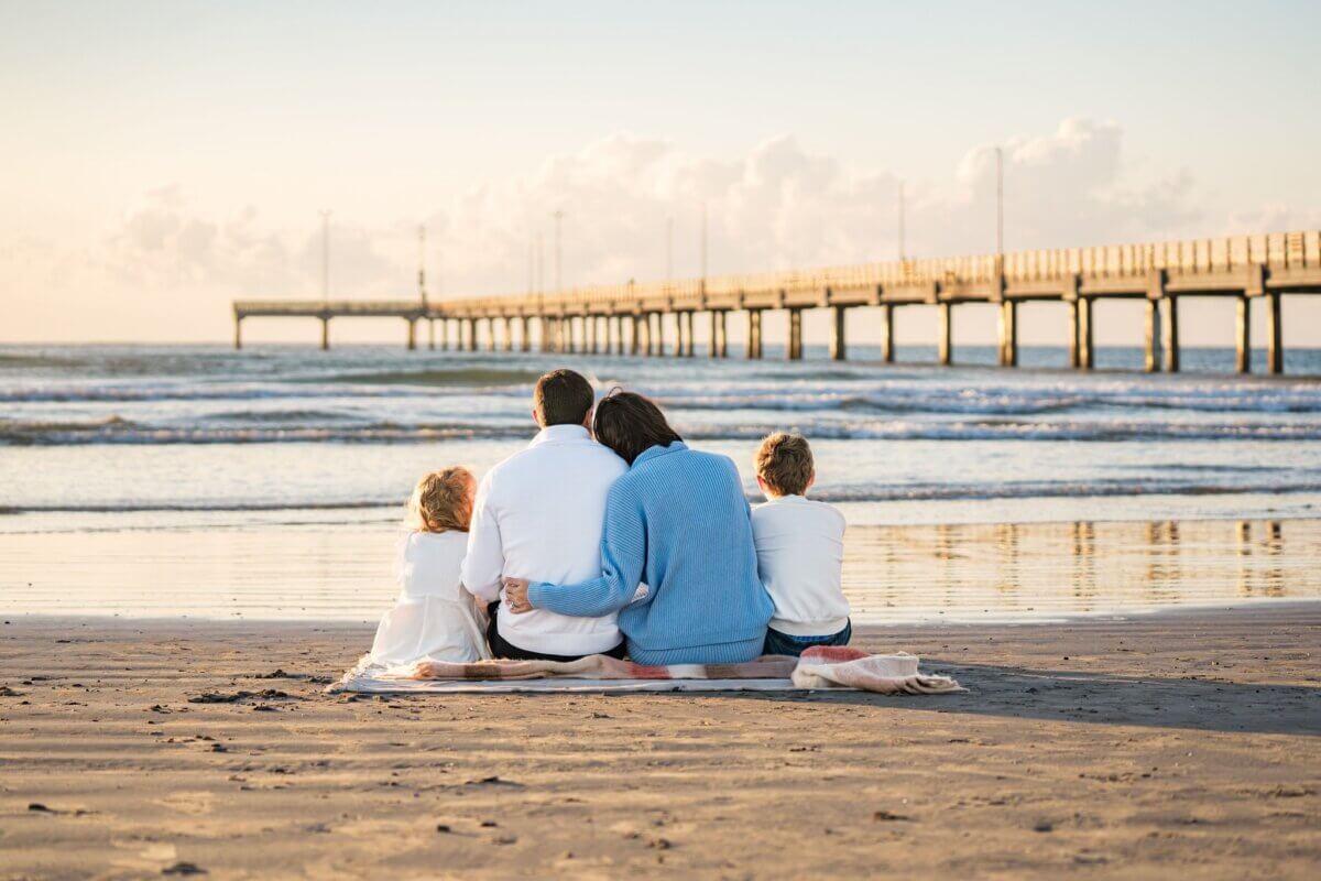 A family of four sits on a blanket at the beach, enjoying a parent-approved sunset with the ocean and pier in the background—one of those classic Southern family vacation destinations.