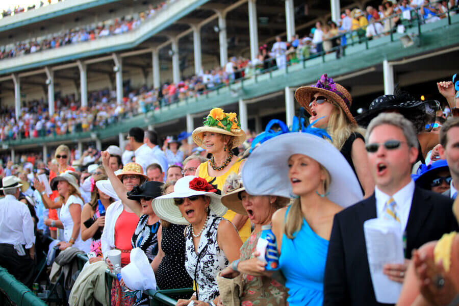 Your Derby 2026 Playbook: What to Know Before You Go - 5 A lively crowd in colorful hats and formal attire cheers at a thrilling Kentucky Derby event in the stadium, capturing the excitement of race day.